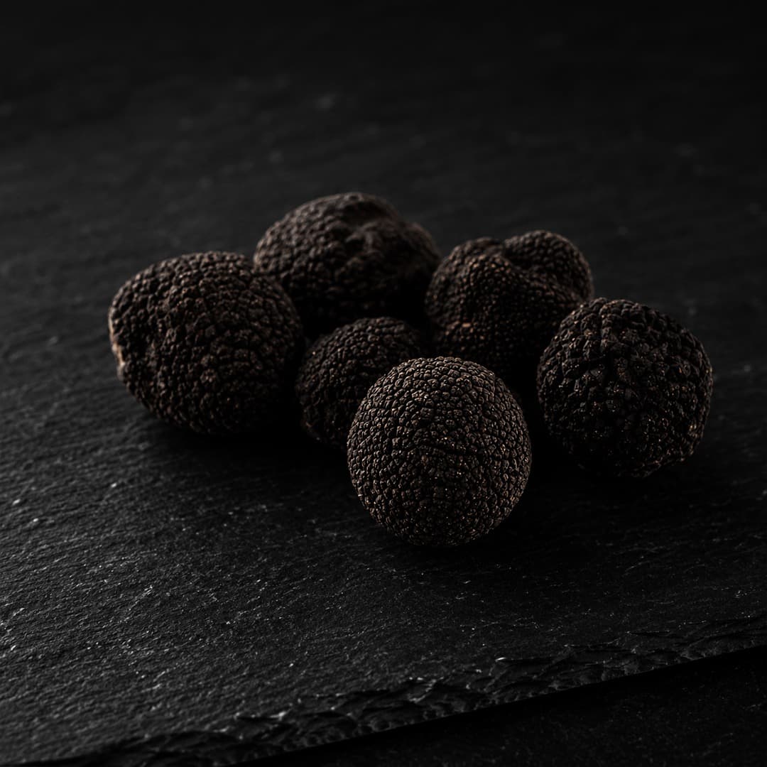 Six black truffles arranged on dark slate